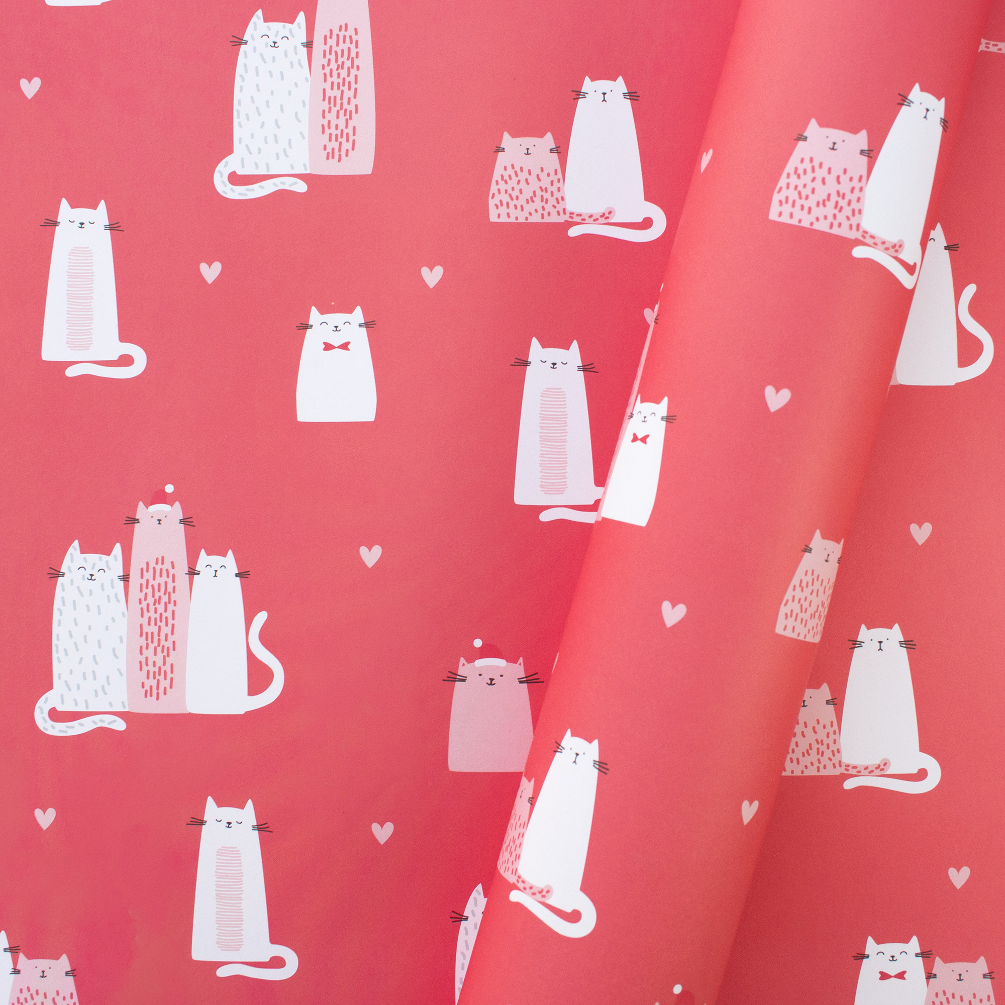 Teilweise eingerolltes Geschenkpapier „Christmas Cats“ mit weißen und rosa Katzen, Weihnachtsmützen und kleinen Herzen auf Korallrot.