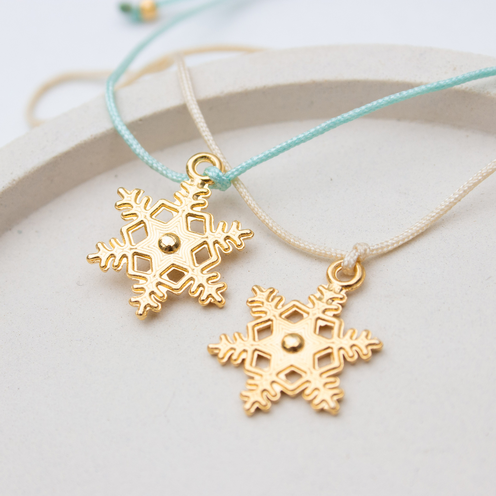 Zwei Weihnachtsarmbänder mit 24 Karat vergoldeter Schneeflocke in den Farben Mint und Creme im direkten Vergleich