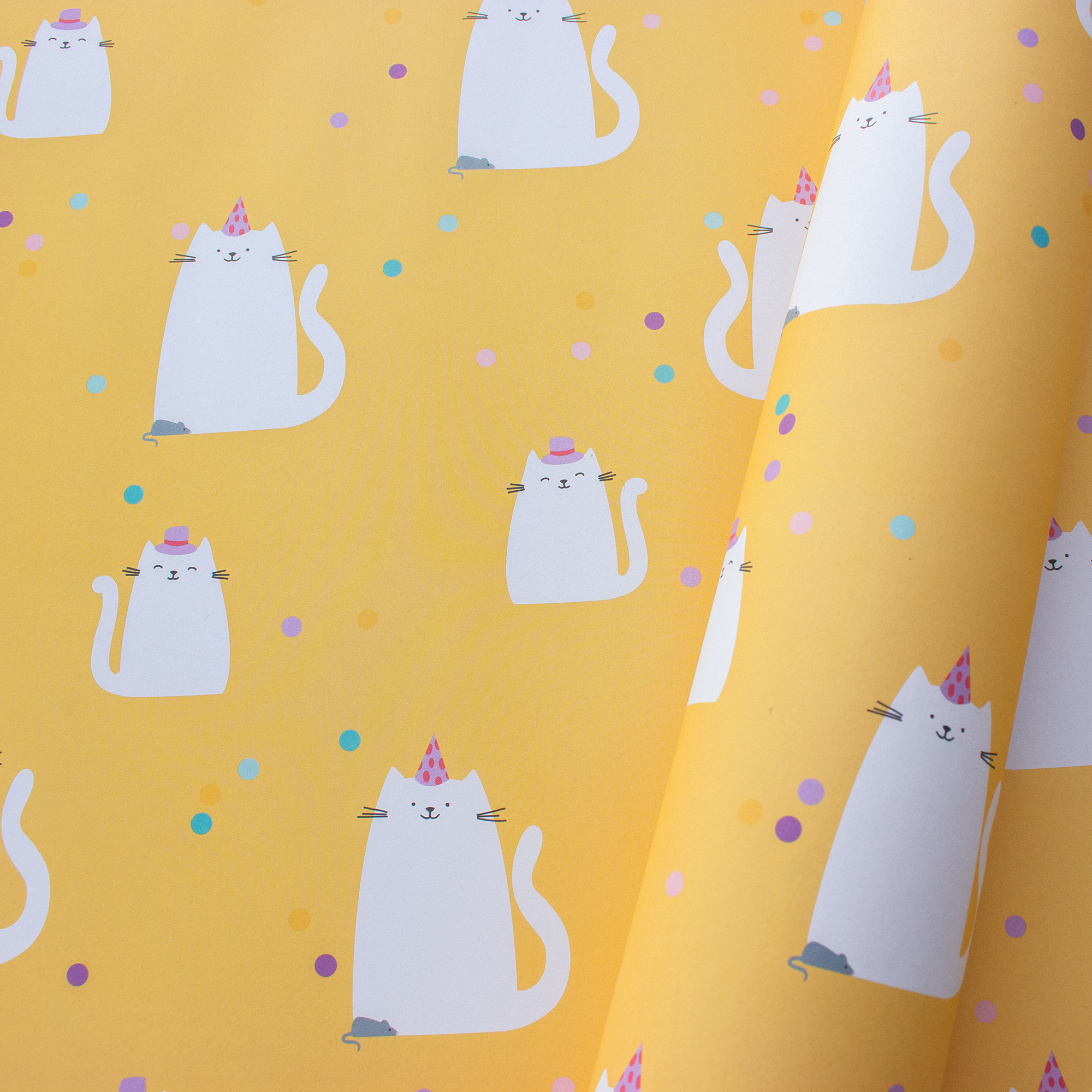 Teilweise eingerolltes Geschenkpapier „Confetti Cats“ mit weißen Katzen, Partyhüten, kleinen Mäusen und buntem Konfetti auf Gelb.