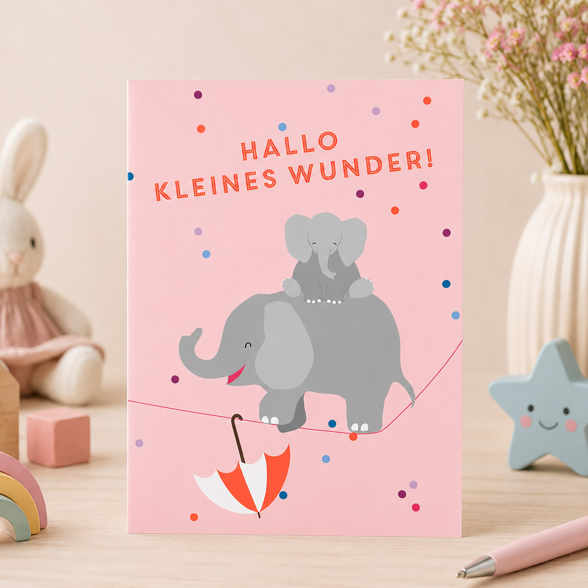 Rosa Karte zur Geburt mit dem Spruch „Hallo kleines Wunder“, zwei Elefanten und bunten Konfetti-Punkten