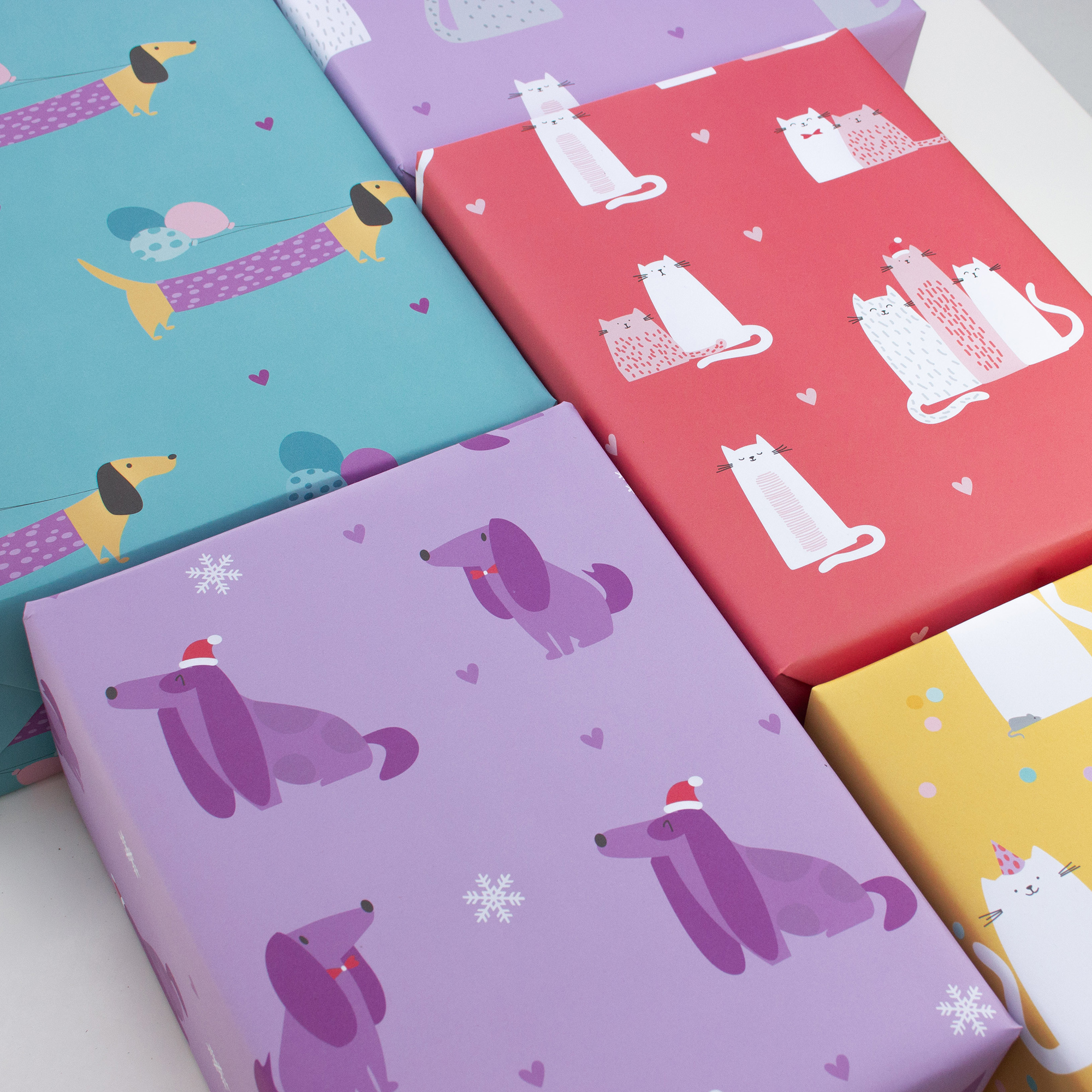 Mehrere Geschenke in Geschenkpapier mit Katzen- und Hundemotiven in Türkis, Flieder, Korallrot und Gelb, mit Geburtstags- und Weihnachtsdetails.