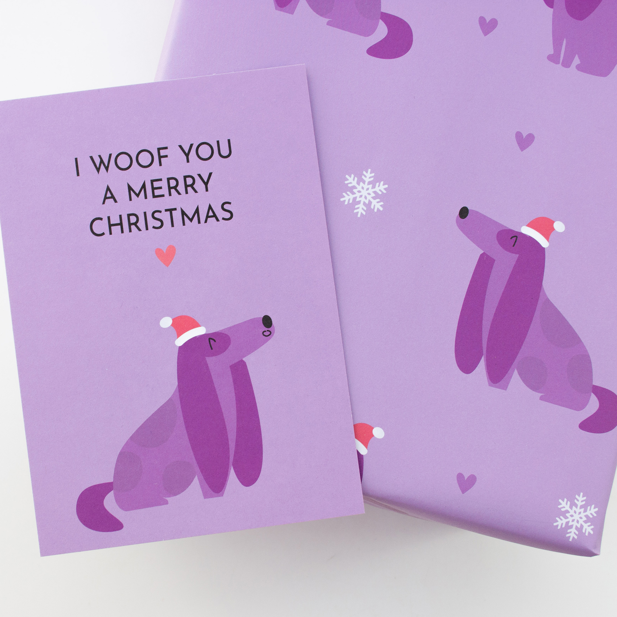 Geschenk in fliederfarbenem Weihnachtspapier mit Hunden und Schneeflocken, dazu die Karte „I woof you a merry Christmas“.