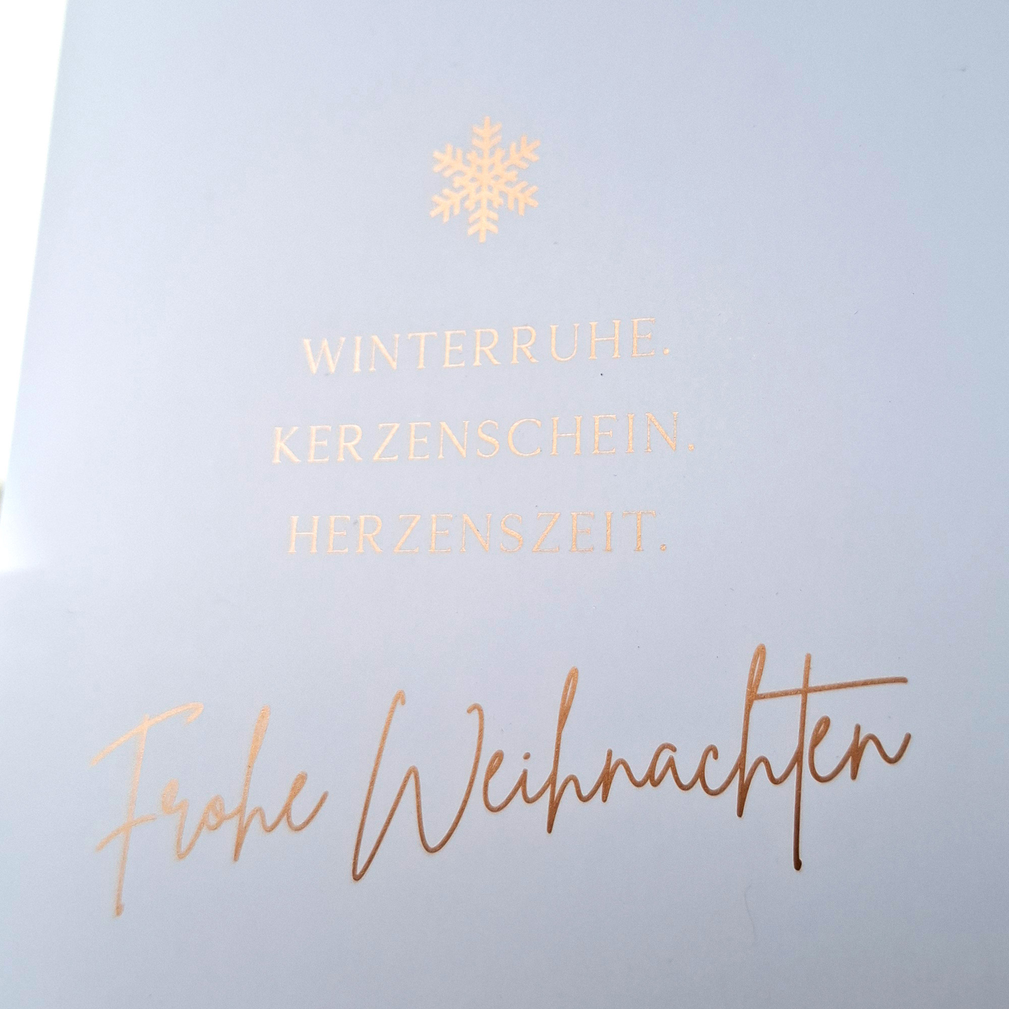 Detail der Weihnachtskarte „Winterruhe. Kerzenschein. Herzenszeit.“ mit Schneeflocke und glänzendem Kupferdruck